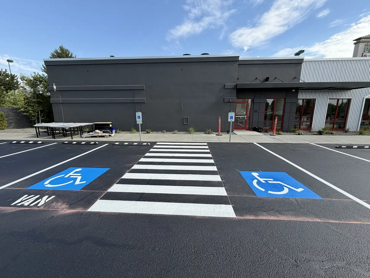 Two ADA van accessible stalls and a white ladder-style crosswalk striped at a commercial building entrance