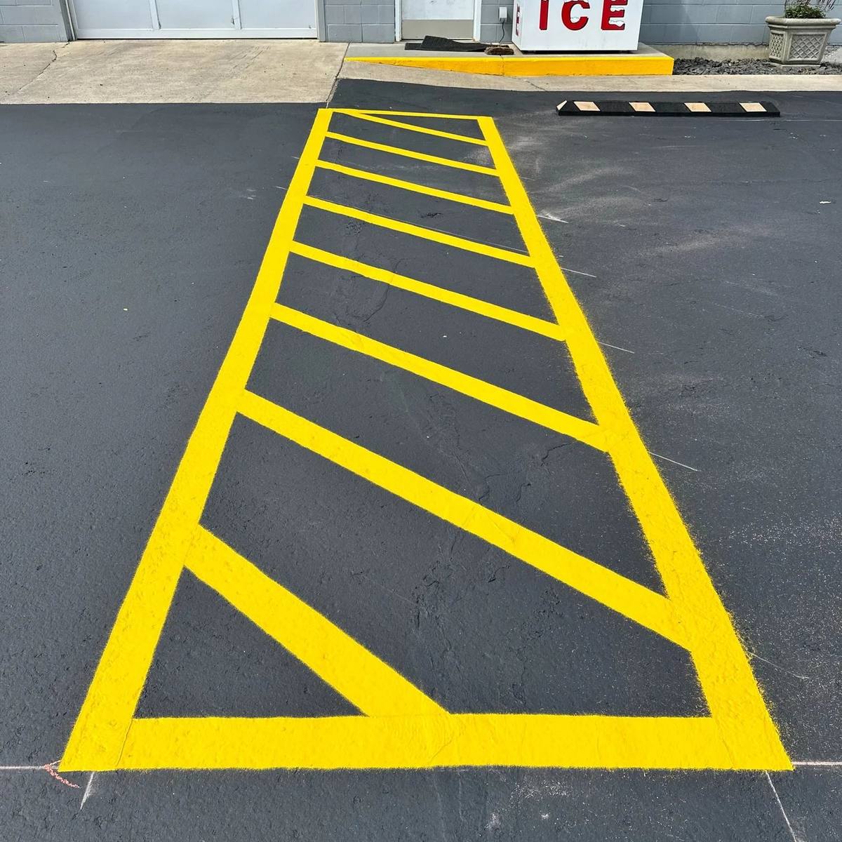 Yellow hazard-striped no-parking area painted on freshly sealcoated black asphalt at a Kennewick commercial property