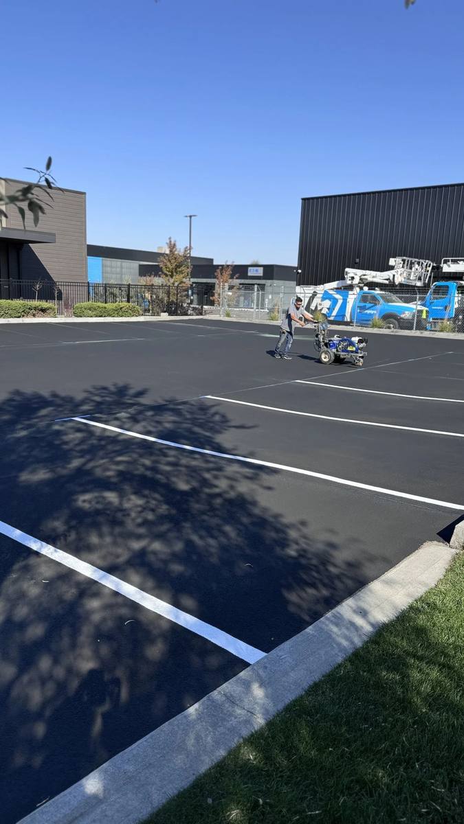 Premier Asphalt Solutions crew member in hi-vis gear operating a line-striping machine on fresh asphalt in the Tri-Cities